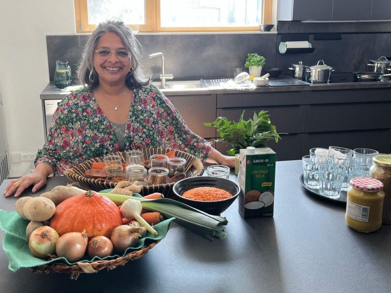Selvi in einer Küche mit Gewürzen, Gemüse und weiteren Zutaten vor sich, um ein leckeres Essen zu zaubern.