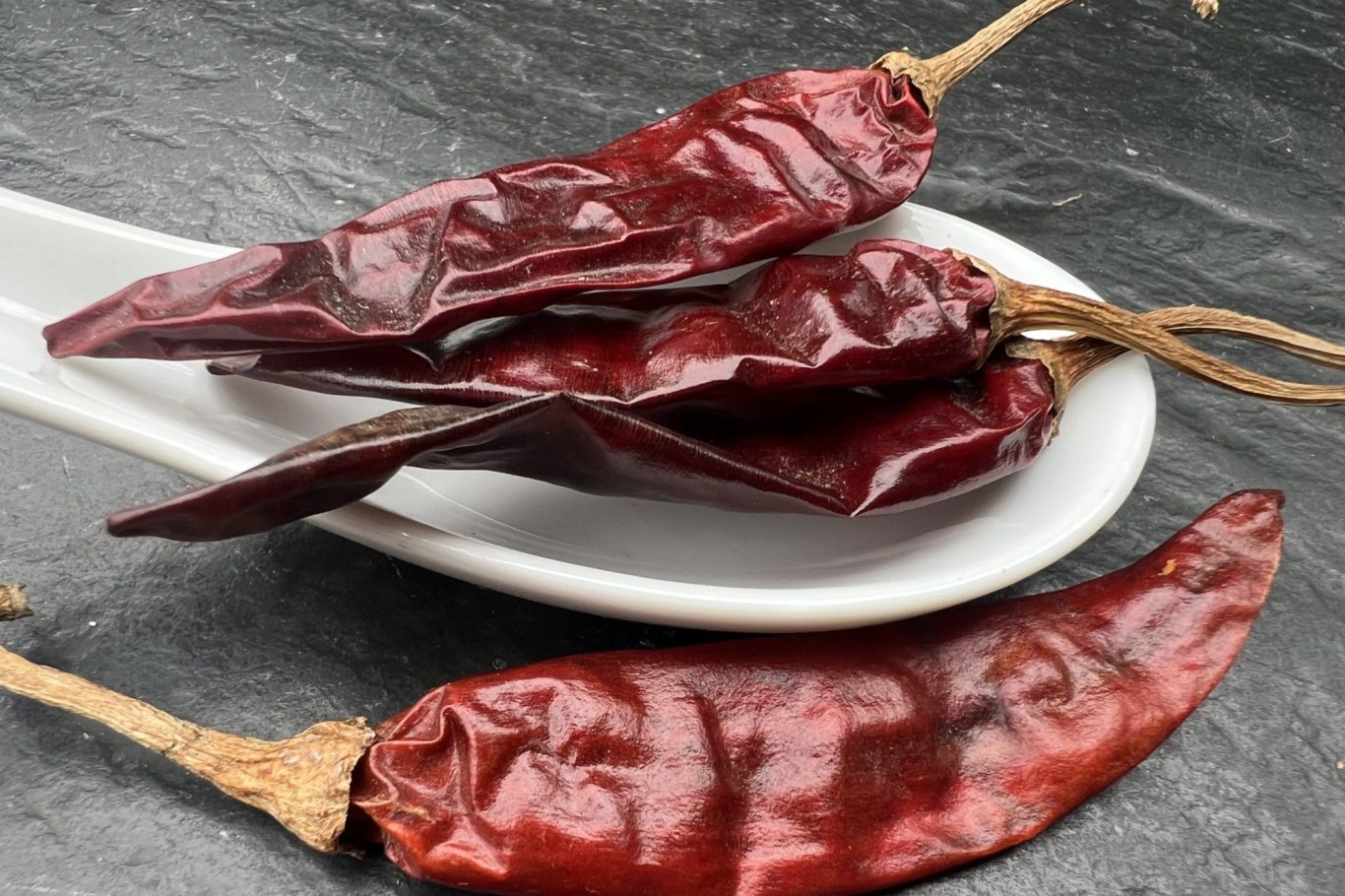 Ein Löffel mit einem Haufen Chilli-schoten und einer davorliegenden Chilli-schote.